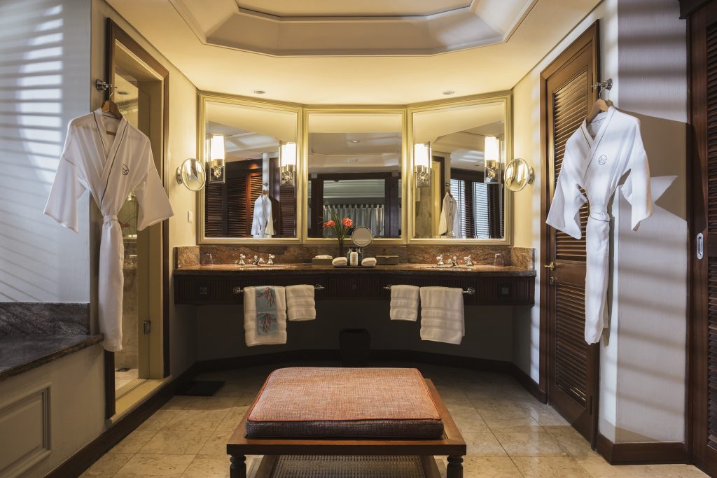 Badezimmer der Junior Suite mit dunklen Holztüren, drei Spiegeln, warmem Licht und gepolsterter Bank