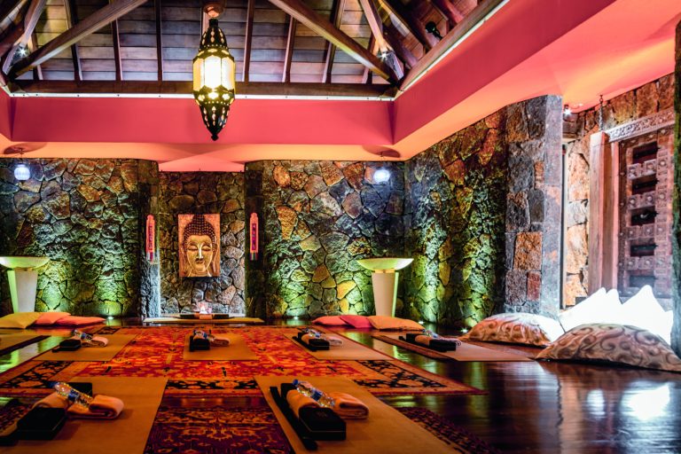 Meditationsraum mit grob behauenen Steinen, bunten Teppichen, Kissen und Buddha-Bild im Dinarobin Beachcomber Golf Resort