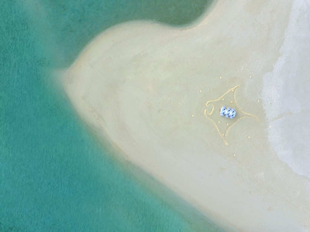 Luftbild einer kleinen Sandbank mit weißem Aufbau und Sandmustern im türkisfarbenen Wasser