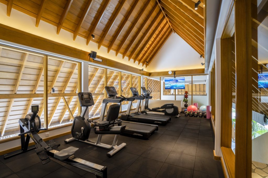 Fitnessraum mit Laufbändern, Rudergerät, Holzdach und großen Fenstern im Emerald Faarufushi Resort & Spa