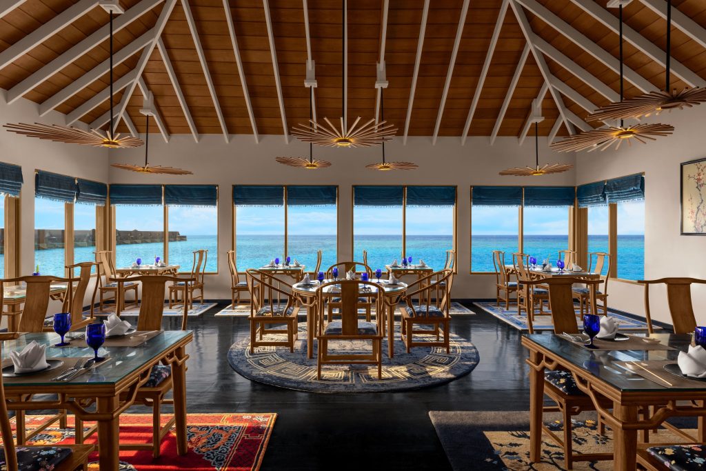 Offener Speisesaal mit Holzmöbeln, gläsernen Tischen und großen Fenstern mit Meerblick im Emerald Faarufushi Resort & Spa