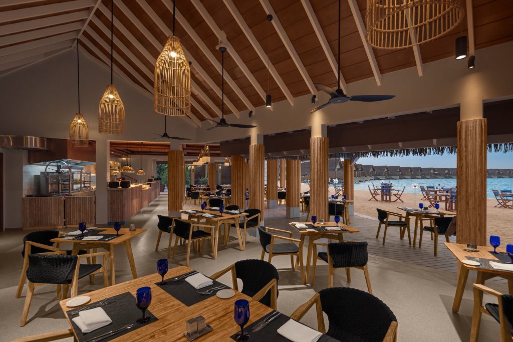 Offener Restaurantbereich im Emerald Faarufushi Resort & Spa mit Holzmöbeln, Dachbalken und Blick auf Strand und Meer