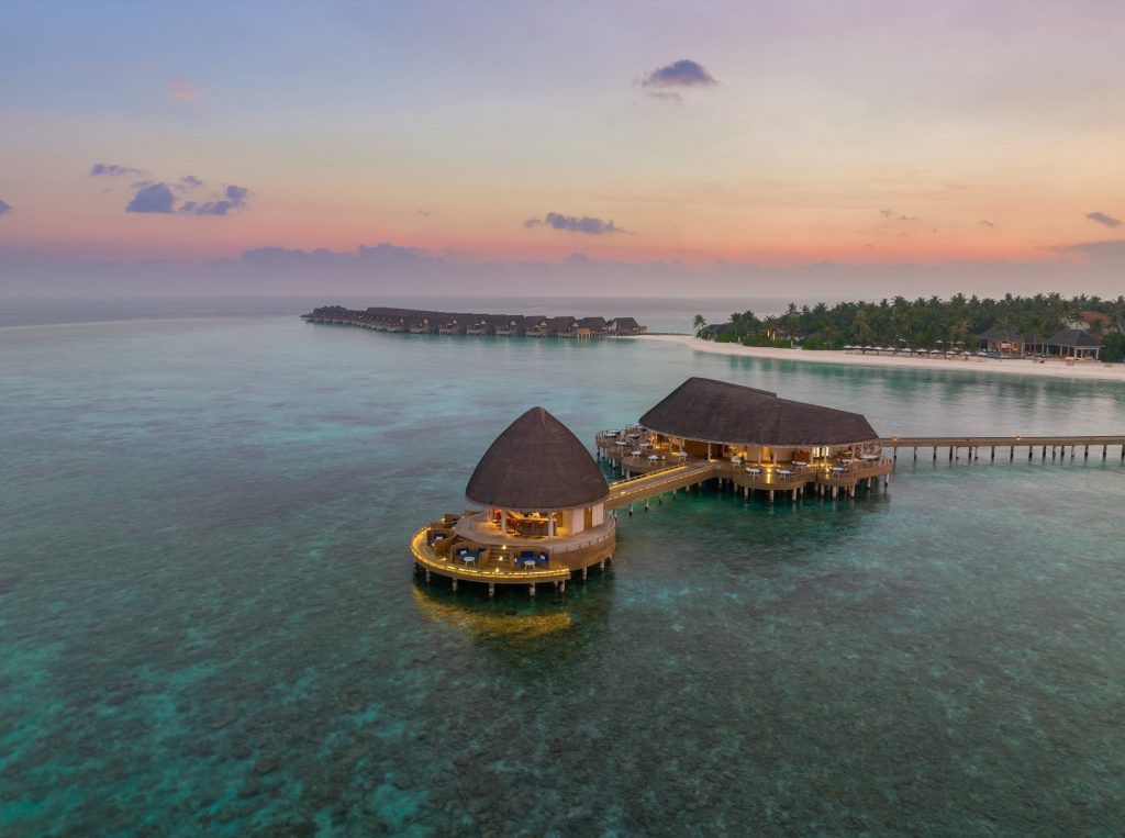 Wasserbungalows auf Pfählen mit Holzdächern und Stroheindeckung über türkisfarbenem Meer bei Abendlicht
