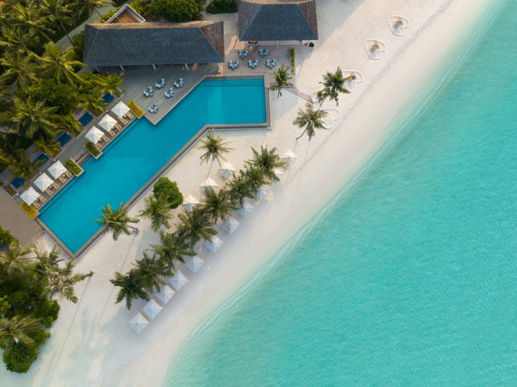 Luftaufnahme des Emerald Faarufushi Resort & Spa Poolbereichs mit Pool, Sonnenschirmen, Palmen und Holzterrassen auf den.