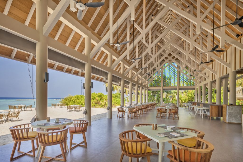 Offener Restaurantbereich im Emerald Faarufushi Resort & Spa mit Holztischen, Dachbalken und Blick auf Strand und Meer