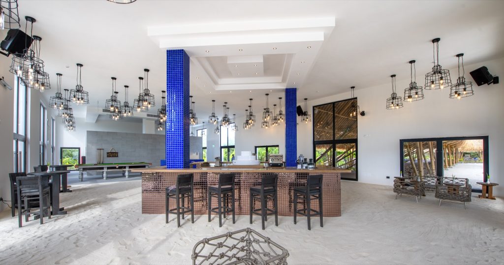 Helle Bar im Emerald Maldives Resort & Spa mit Holztheke, schwarzen Hockern und blauer Wand