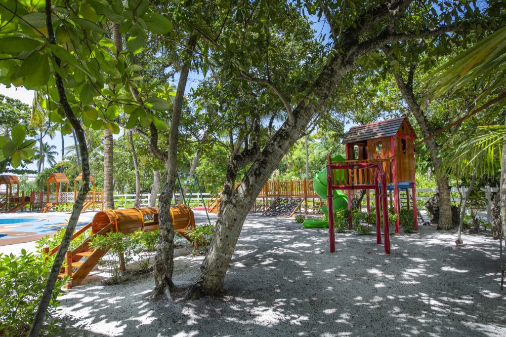 Spielplatz mit roten und natürlichen Holzspielgeräten und grüner Rutsche in tropischem Garten auf den