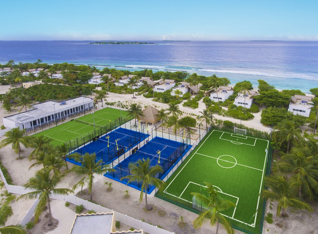Hotelgelände mit zwei blauen Tennisplätzen, grünem Fußballplatz, Bungalows und Hauptgebäude auf den