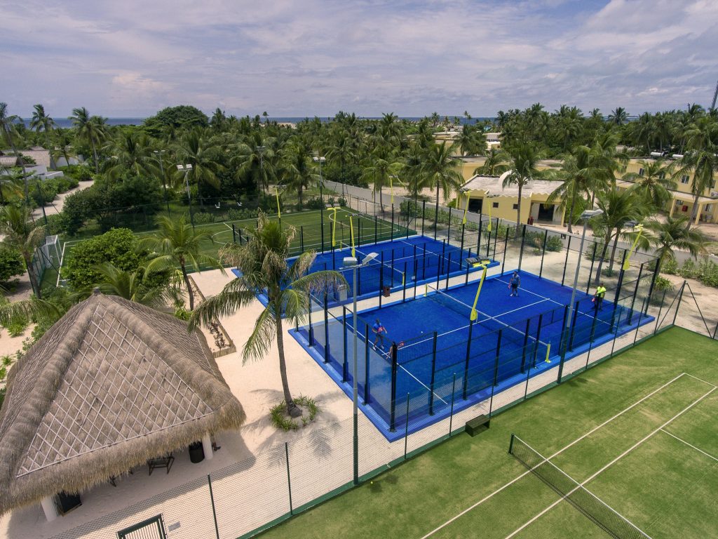 Padeltennisplatz mit Glas- und Metallbegrenzung, Pavillon aus Holz und Palmblättern, grüner Rasen bei Tageslicht