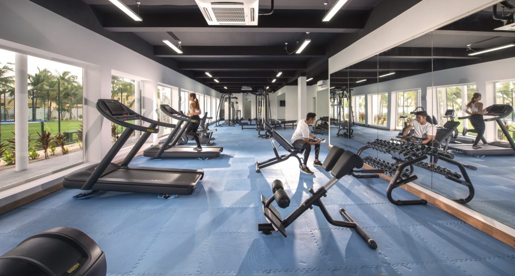 Moderner Fitnessraum im Emerald Maldives Resort & Spa mit Laufbändern, Hantelbänken, blauer Matte und großen Fenstern