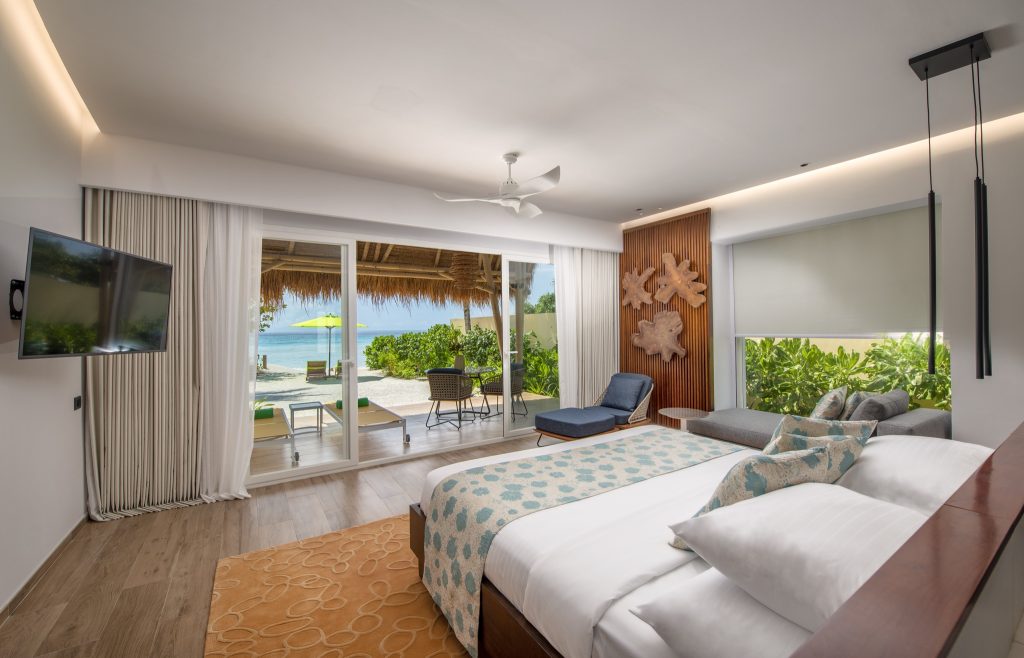 Modernes Hotelzimmer mit großem Bett, blauem Sessel, Holzdekoration und Meerblick durch Glasfront