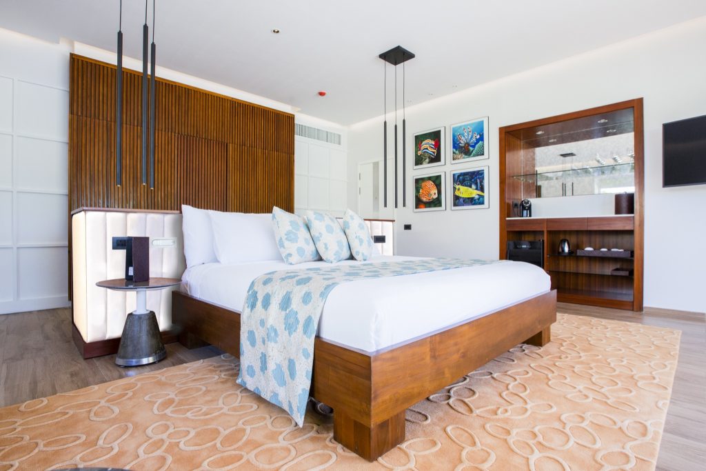 Modernes Hotelzimmer der Beach Villa mit großem Bett, Holzrahmen, blauen Mustern und Holzregal