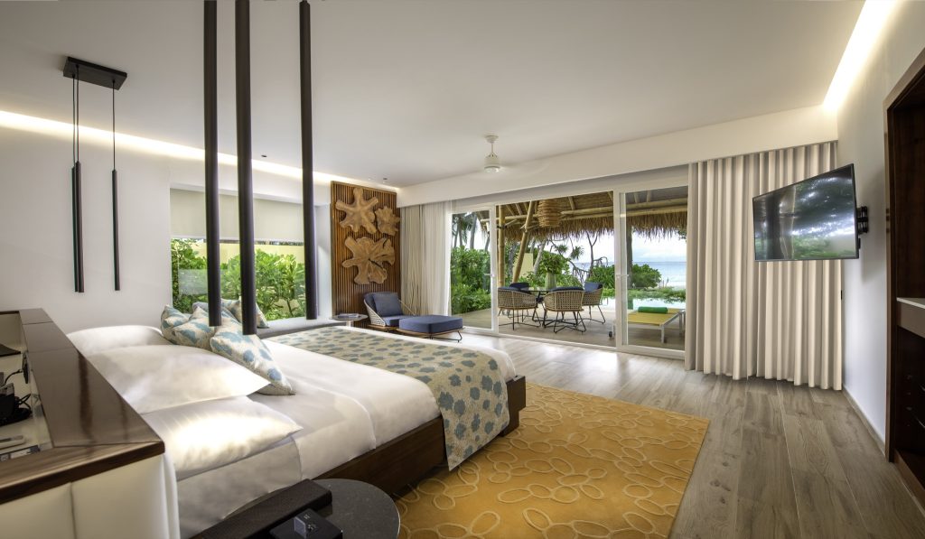 Modernes Zimmer der Beach Villa mit Doppelbett, Holzreliefs, Rattanmöbeln und Meerblick auf den