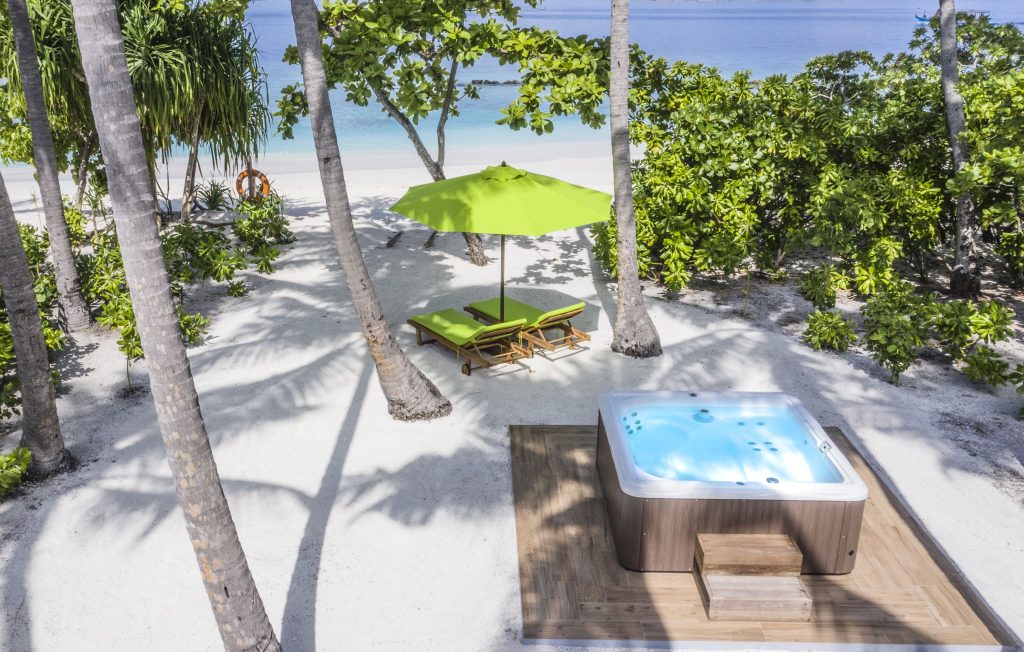 Whirlpool auf Holzplattform mit zwei grünen Liegestühlen und Sonnenschirm am Strand im Emerald Maldives Resort & Spa