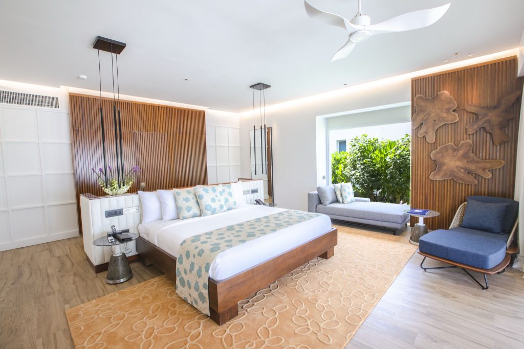 Modernes Hotelzimmer im Emerald Maldives Resort & Spa mit großem Bett, Holzrahmen und natürlichem Licht