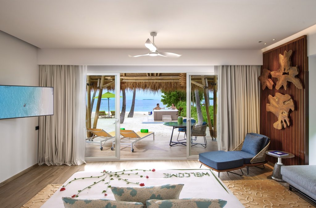 Modernes Hotelzimmer im Emerald Maldives Resort & Spa mit Bett, Holzboden und direktem Zugang zur Strandterrasse.