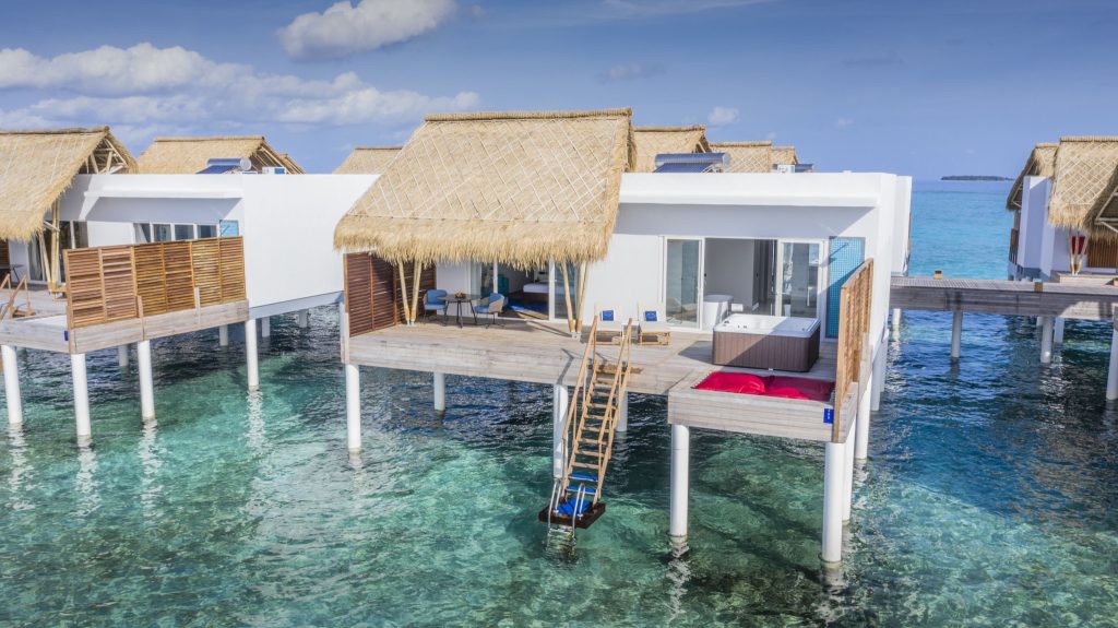 Über dem Wasser gebautes Bungalow mit Reetdach, Holzterrasse und modernen Außenmöbeln im Emerald Maldives Resort & Spa
