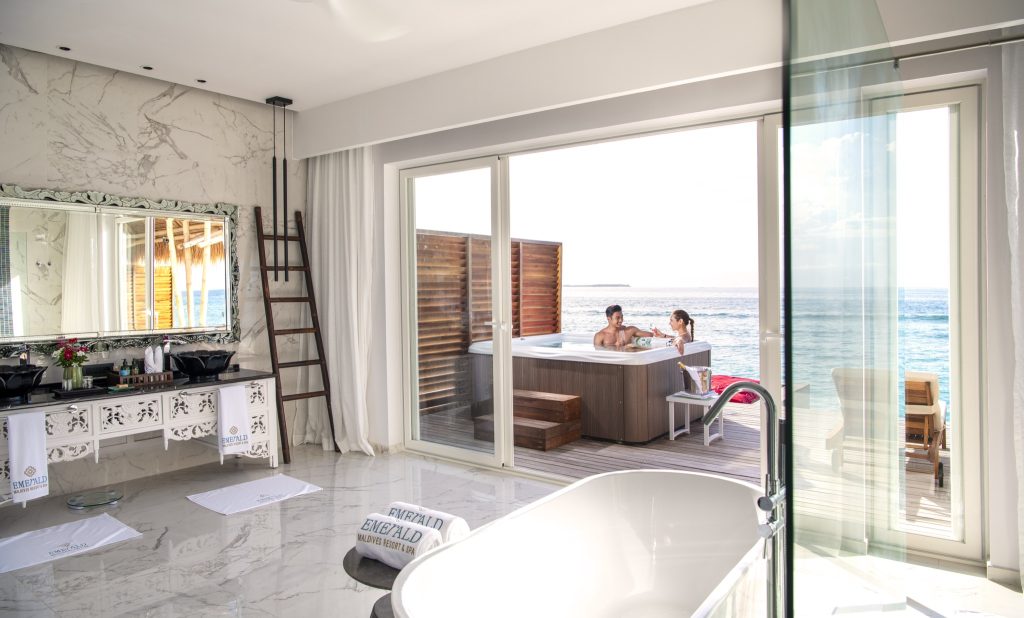 Badezimmer mit marmorierten Wänden, großem Spiegel, Kommode und Blick auf Terrasse mit Whirlpool und Meer im Emerald.