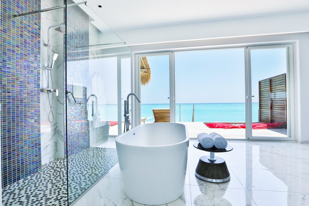 Modernes Badezimmer mit freistehender weißer Badewanne, Mosaikfliesen und Meerblick im Emerald Maldives Resort & Spa