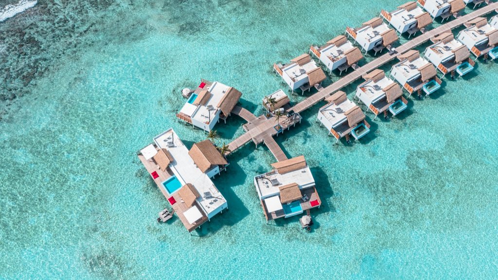 Wasserbungalows mit strohgedeckten Dächern und Holzstegen über türkisfarbenem Ozean im Emerald Maldives Resort & Spa