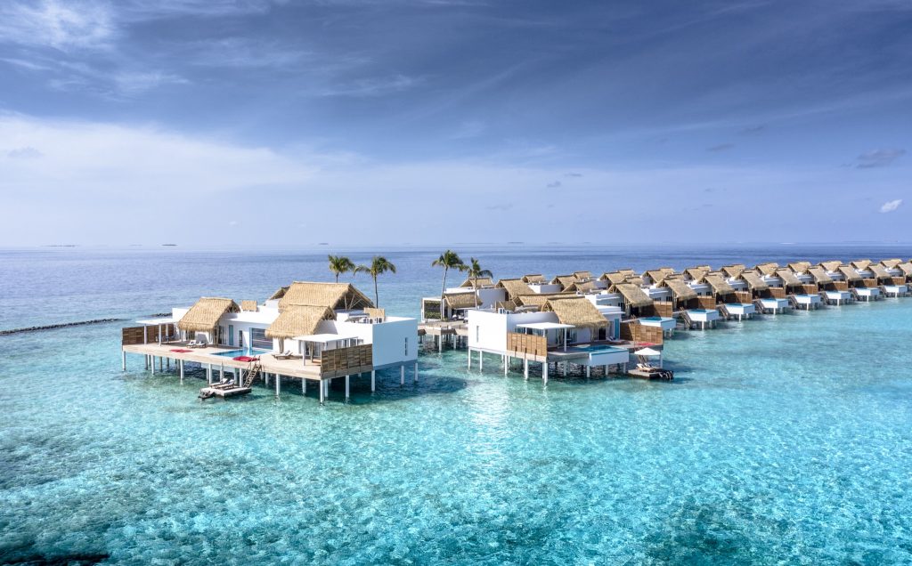 Reihe von weißen Überwasser-Bungalows mit hellbraunen Strohdächern auf Stelzen im türkisblauen Meer bei Tageslicht