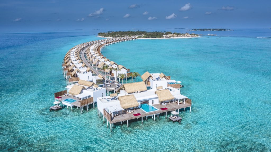 Reihe von weißen Überwasserbungalows mit Strohdächern an einem Steg über türkisblauem Wasser auf den
