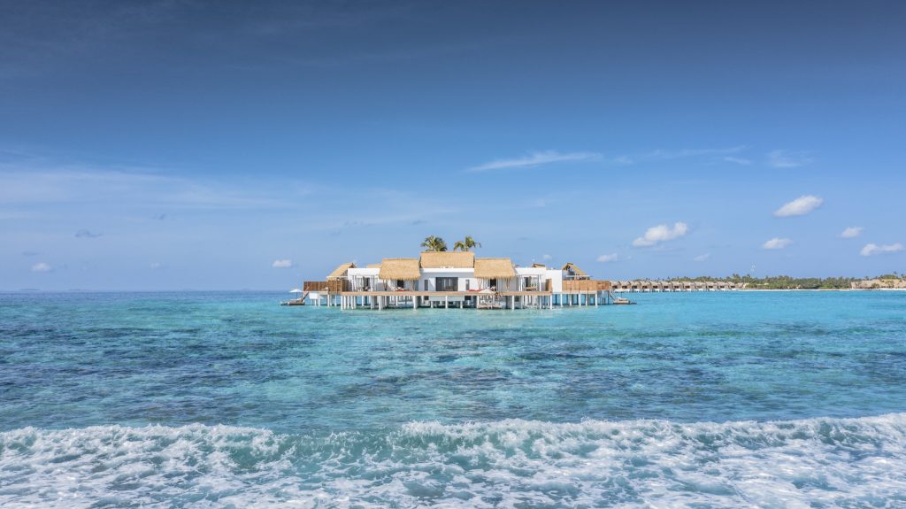 Modernes Hotel auf Pfählen über türkisfarbenem Ozean mit weißen Pavillons und Strohdächern im Emerald Maldives Resort & Spa