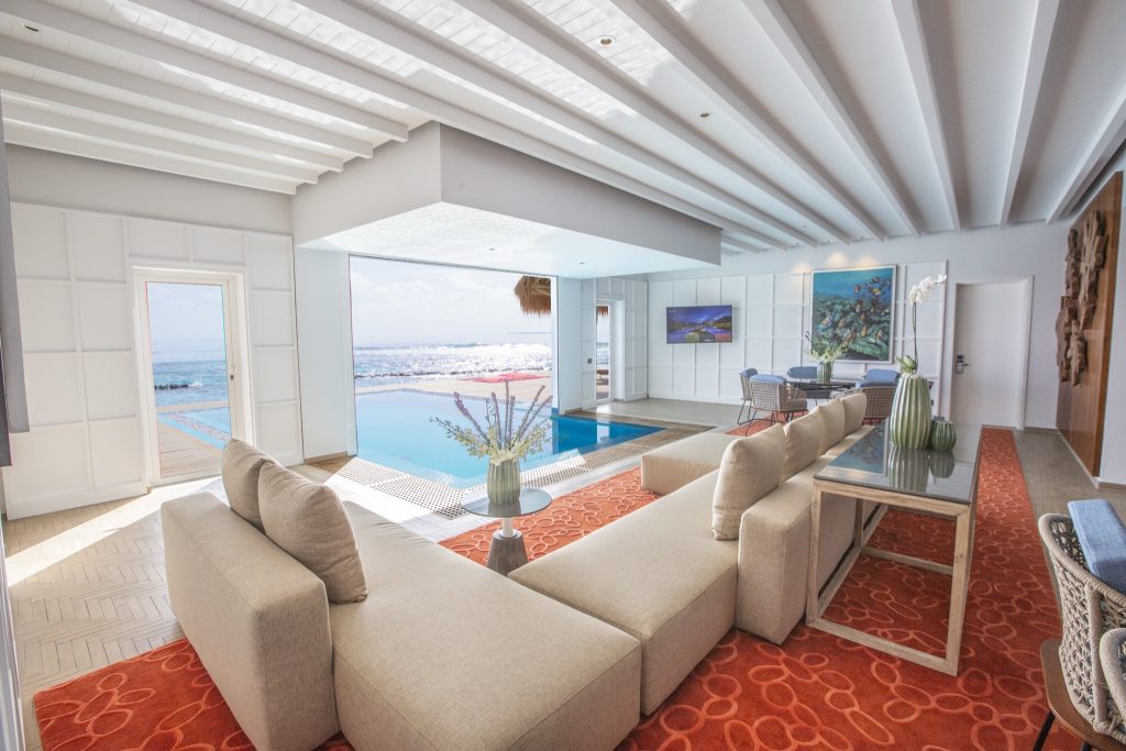 Zimmer der Presidential Water Villa mit beigen Polstermöbeln, rotem Teppich und Meerblick vom Emerald Maldives Resort & Spa