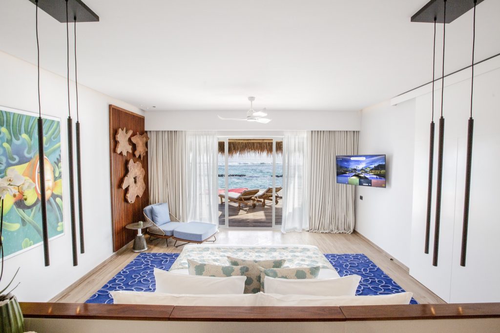 Modernes Hotelzimmer mit blauer Teppich, heller Couch, Holzverkleidung und Meerblick durch große Schiebetüren