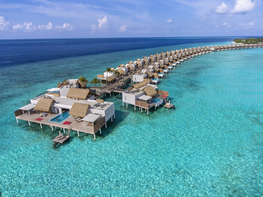 Reihe von Wasserbungalows mit Strohdächern und weißem Anstrich auf Stelzen über türkisfarbenem Meer mit privatem Pool
