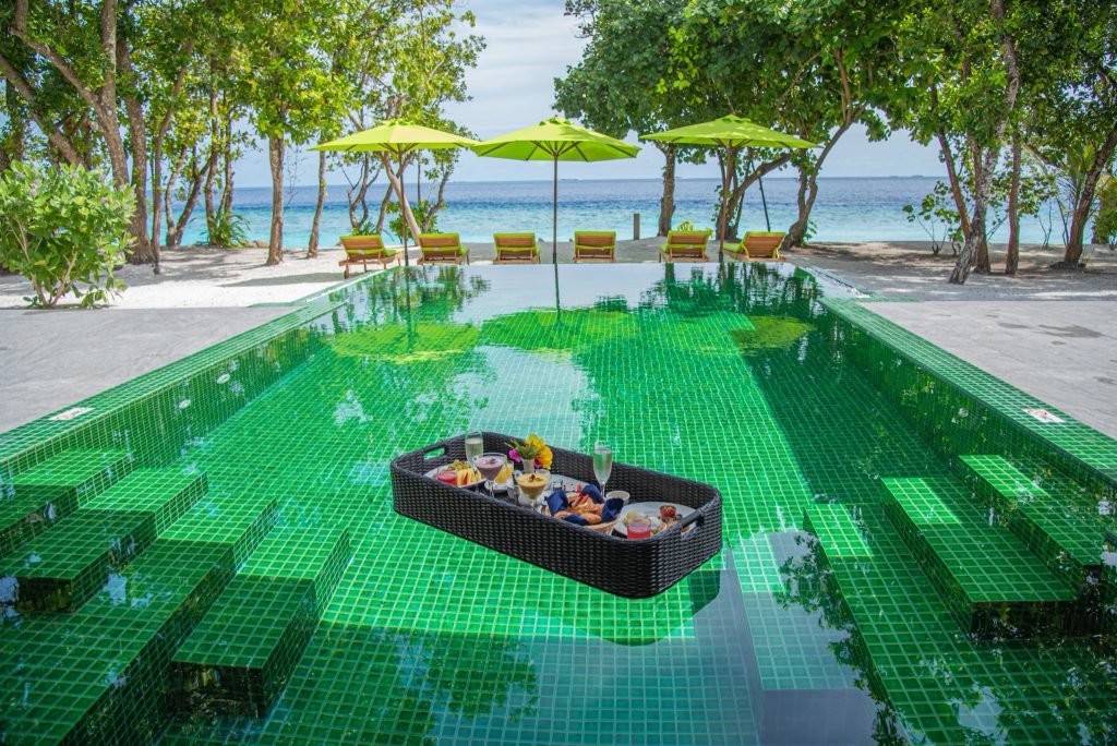 Rechteckiger Swimmingpool mit grünen Kacheln, Holzziegenstühlen, Sonnenschirmen und Meerblick im Emerald Maldives Resort &.