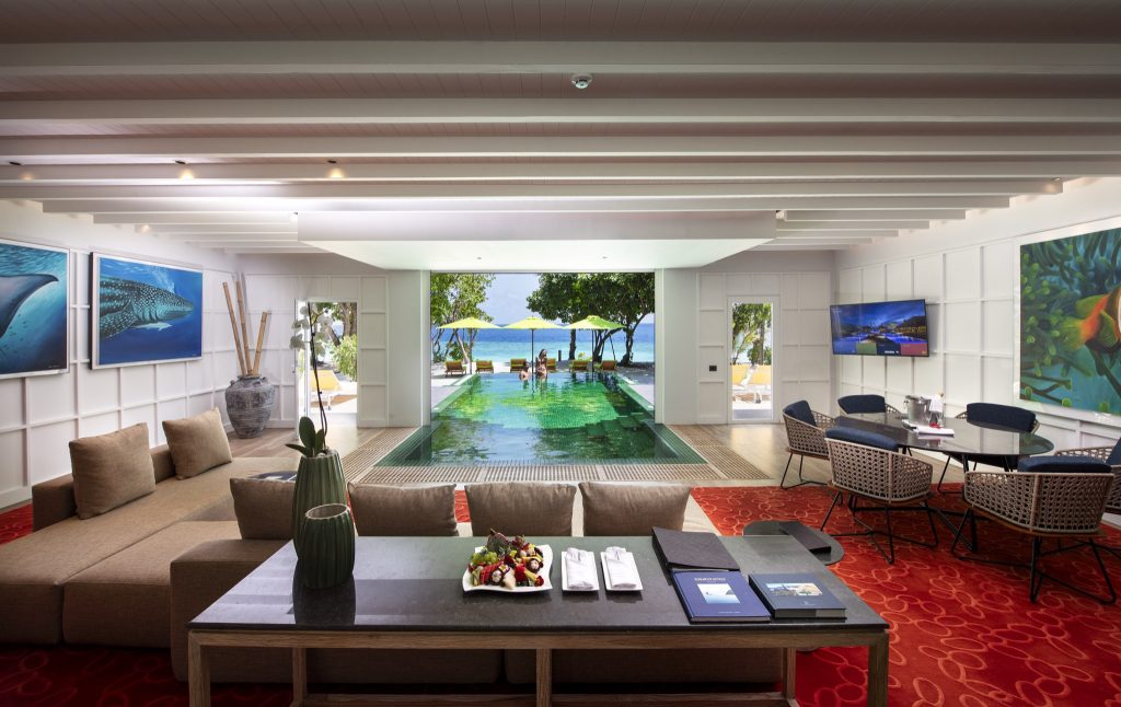 Offener Hotelraum Royal Beach Villa mit Sofaecke, dunklem Holztisch und Blick auf Pool und Küste im Emerald Maldives Resort.
