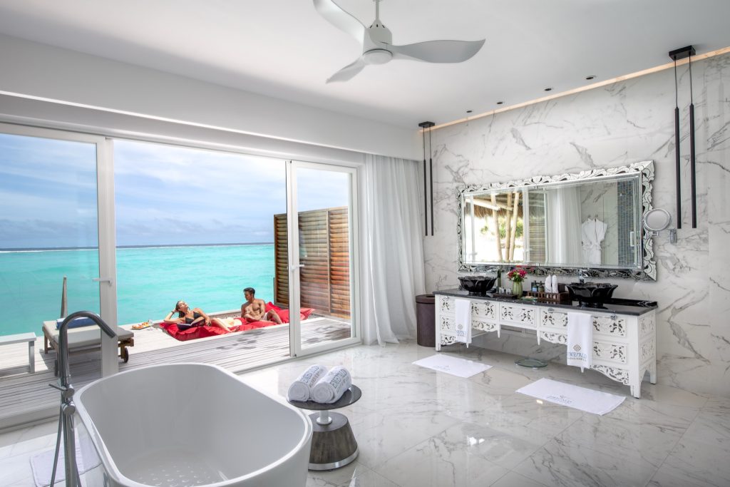 Modernes Badezimmer mit freistehender Badewanne, weißem Marmor und großem Spiegel, Blick auf Meer und Terrasse