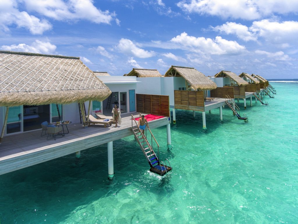 Reihe von Water Villas mit Palmwedeldächern und Holzterrassen über türkisfarbenem Meer auf den