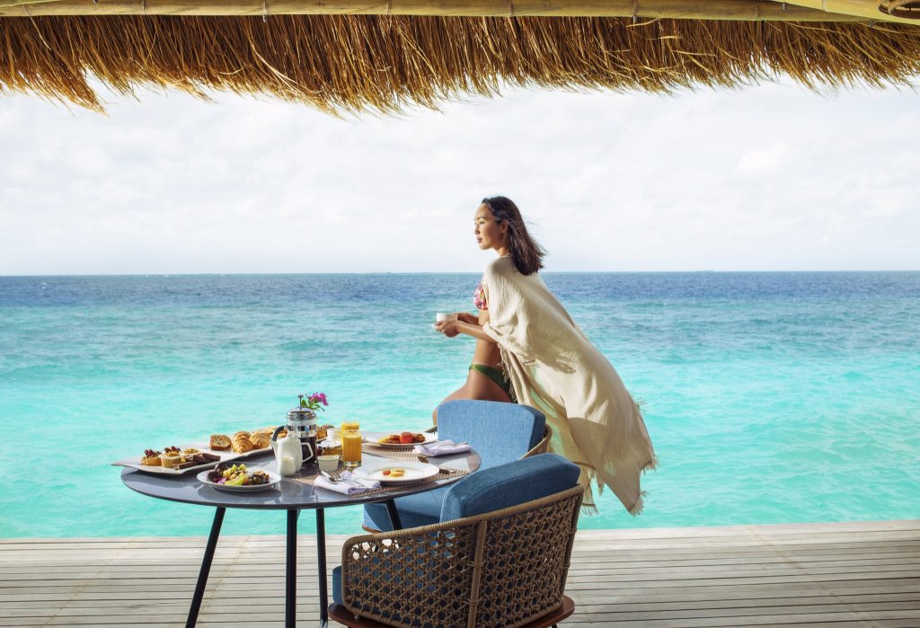 Runder Frühstückstisch mit Gebäck, Obst und Getränken auf Holzterrasse mit Blick auf das blaue Meer im Emerald Maldives.