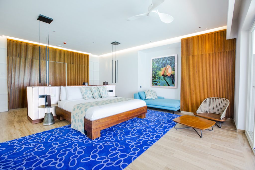 Modernes Water Villa Zimmer im Emerald Maldives Resort & Spa mit Holzrahmenbett, blauem Sofa und Teppich