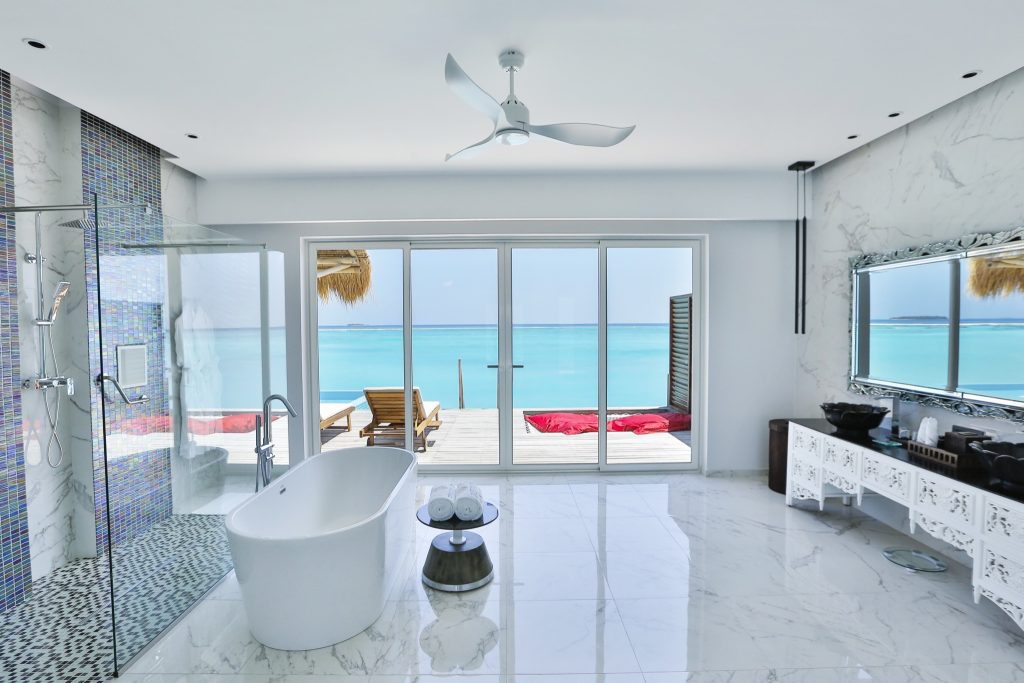 Modernes Badezimmer der Water Villa mit freistehender Badewanne, Glasdusche, Marmorfliesen und Meerblick im Emerald Maldives.