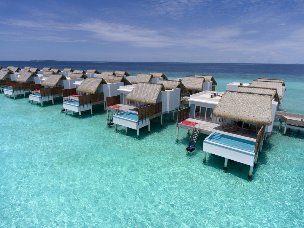 Überwasser-Bungalows mit Strohdächern und weißen Wänden auf klarem blauem Wasser im Emerald Maldives Resort & Spa