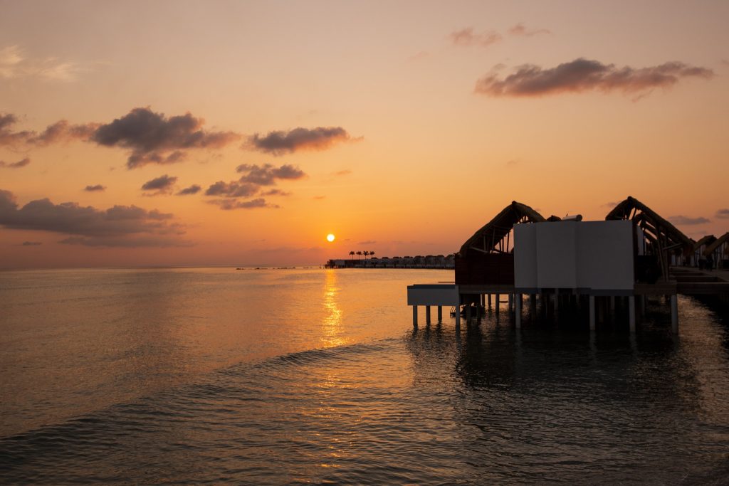 Reihe von Water Villas mit Pool auf Pfählen im Meer bei Sonnenuntergang im Emerald Maldives Resort & Spa