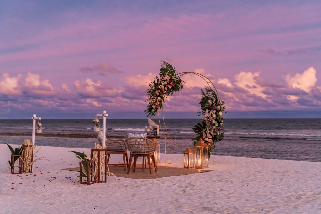 Am Strand arrangierter Holztisch für zwei mit Metallkreis und roten Blütenblättern bei Sonnenuntergang