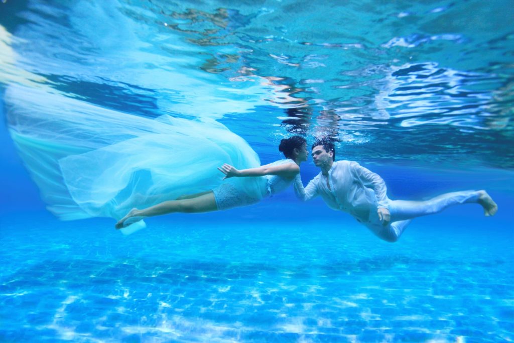 Paar unter Wasser im Schwimmbecken des Four Seasons Resort Maldives at Kuda Huraa mit blau-türkisfarbenem Licht