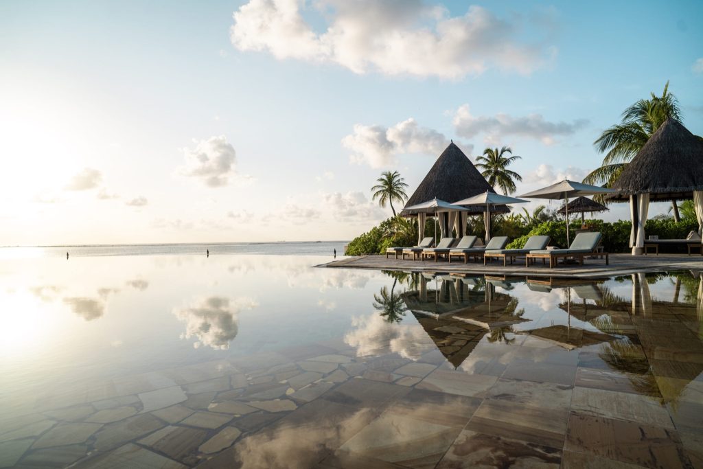 Infinity-Pool mit Strohdach-Pavillons, Liegestühlen, Steinplatten und Meerblick im Four Seasons Resort Maldives