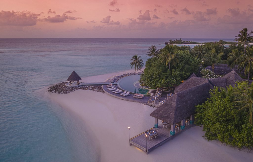 Runder Infinity-Pool mit Liegen, Holzsteg und Pavillon am weißen Sandstrand der Malediven bei Abenddämmerung