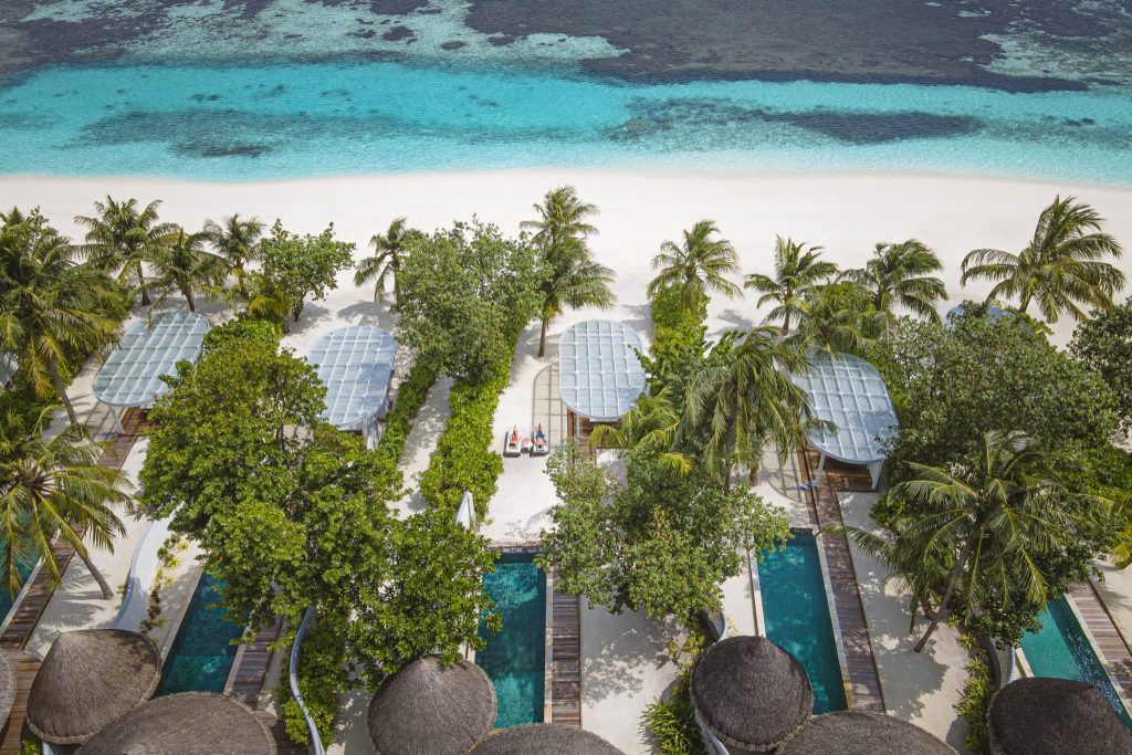Luftaufnahme von Bungalows mit wellenförmigen Dächern, Pools, Palmen und türkisfarbenem Meer auf den