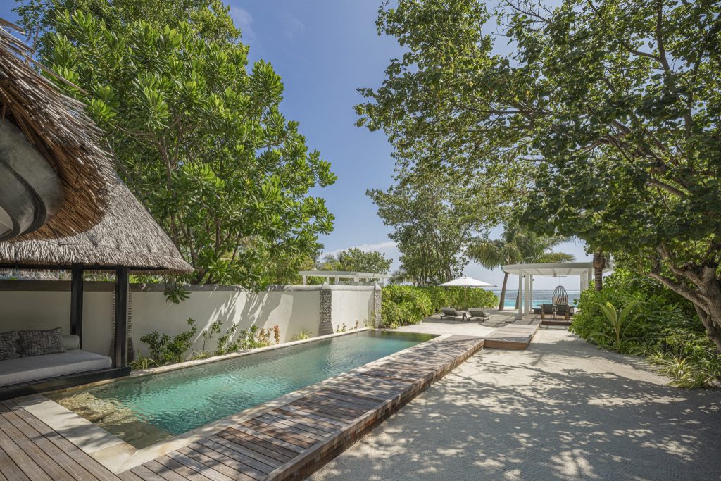 Außenbereich mit rechteckigem Pool, Holzdeck, Strohdach-Sitzgelegenheit und üppigem Grün im Four Seasons Resort Maldives at.