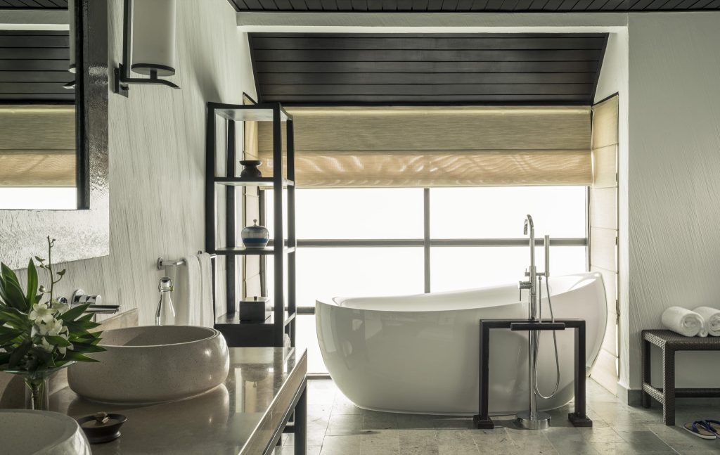 Badezimmer mit freistehender weißer Badewanne, Steinwaschbecken, Marmortresen und großem Fenster