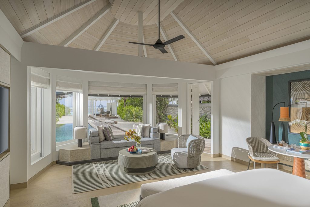 Hotelzimmer mit hoher Holzdecke, Sofa, großen Fenstern und Terrasse mit Pool und Garten auf den