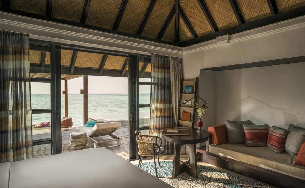 Zimmer der Sunset 3BR Water Suite mit Bett, Sitzecke, Glasfront und Terrasse mit Meerblick