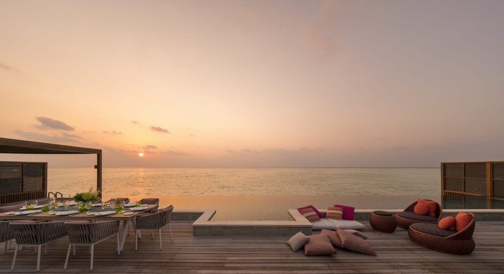 Terrasse mit Esstisch, Pool und Sitzgelegenheiten bei Sonnenuntergang im Four Seasons Resort Maldives at Kuda Huraa