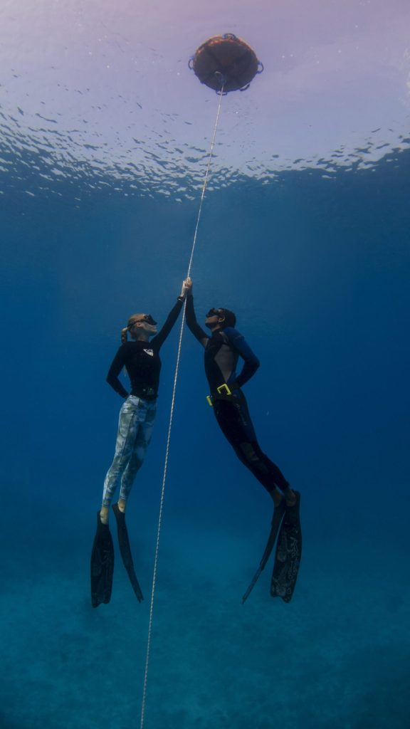 Zwei Taucher mit Ausrüstung halten sich an einem Seil unter Wasser mit Boje